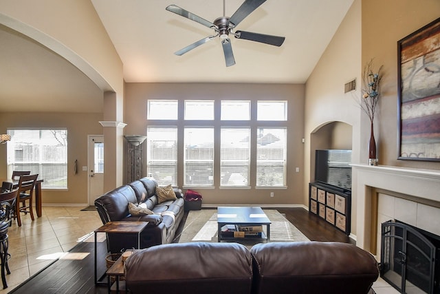 tiled living area featuring visible vents, a ceiling fan, a tiled fireplace, arched walkways, and baseboards