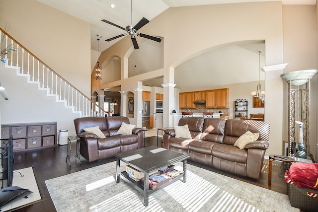 living room featuring stairway, wood finished floors, ornate columns, high vaulted ceiling, and ceiling fan with notable chandelier