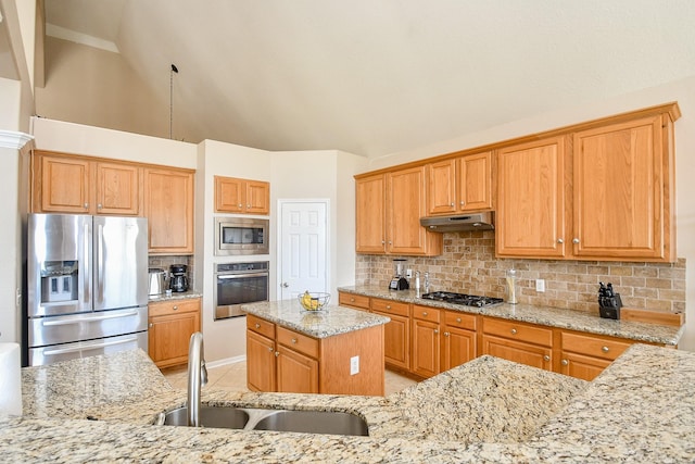 kitchen featuring a sink, under cabinet range hood, appliances with stainless steel finishes, decorative backsplash, and light stone countertops