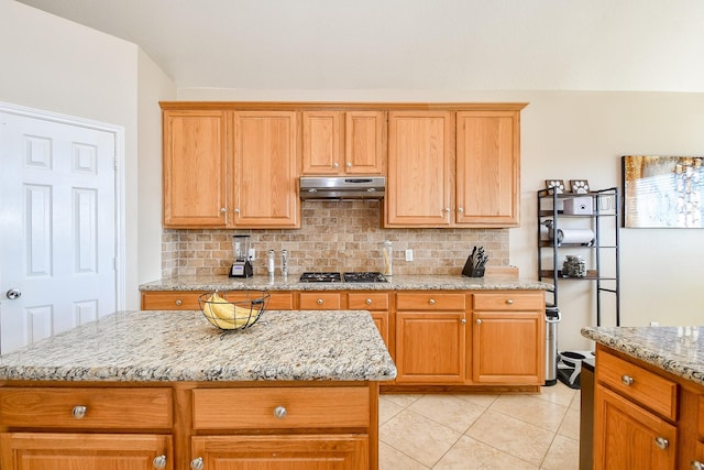 kitchen featuring under cabinet range hood, decorative backsplash, stainless steel gas cooktop, and light stone counters