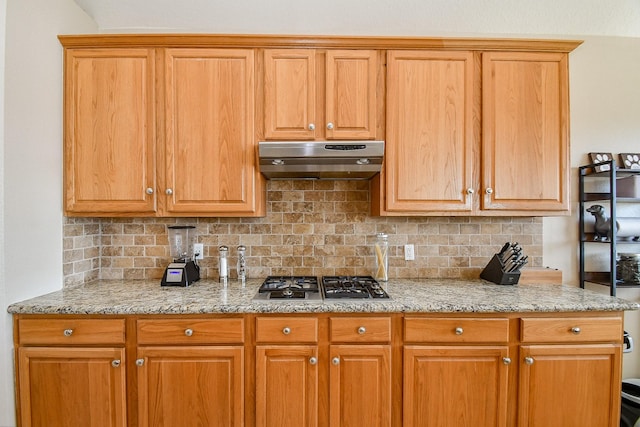 kitchen featuring light stone countertops, tasteful backsplash, under cabinet range hood, and stainless steel gas cooktop