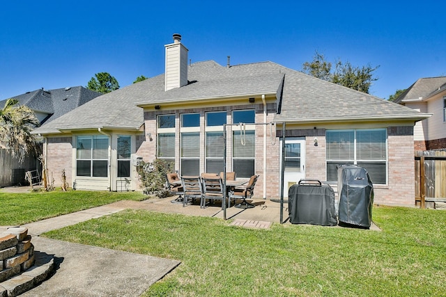 back of property with a yard, brick siding, a chimney, and fence