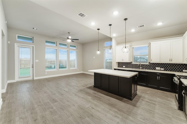 kitchen with a sink, visible vents, dark cabinetry, a ceiling fan, and a kitchen island