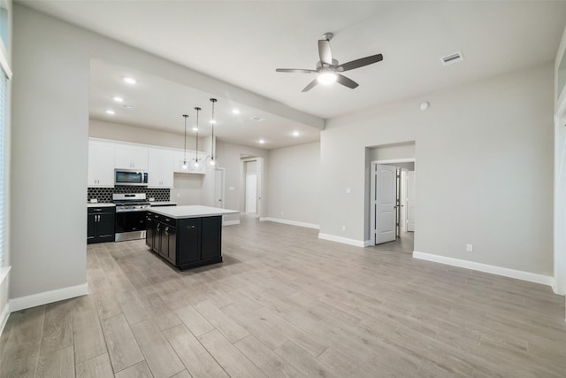 kitchen featuring light wood finished floors, a ceiling fan, dark cabinetry, appliances with stainless steel finishes, and open floor plan