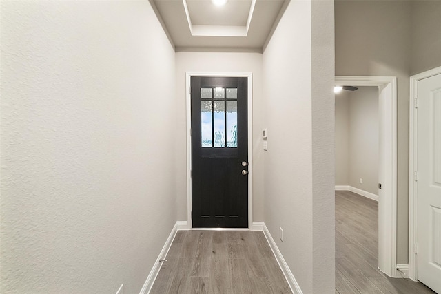 doorway to outside featuring baseboards, wood finished floors, and a raised ceiling