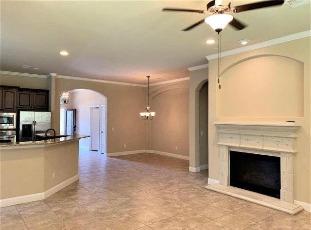 kitchen featuring a fireplace with raised hearth, arched walkways, ornamental molding, appliances with stainless steel finishes, and ceiling fan with notable chandelier