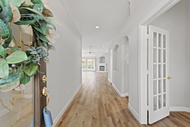 hall with baseboards, light wood-style flooring, recessed lighting, arched walkways, and crown molding