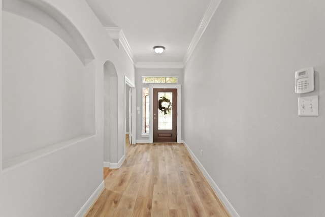 doorway with arched walkways, light wood-style flooring, crown molding, and baseboards