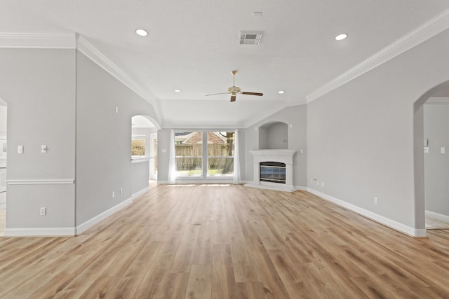 unfurnished living room featuring visible vents, light wood-style flooring, a glass covered fireplace, arched walkways, and crown molding