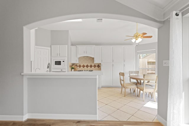 kitchen featuring white microwave, backsplash, light countertops, white cabinetry, and a ceiling fan