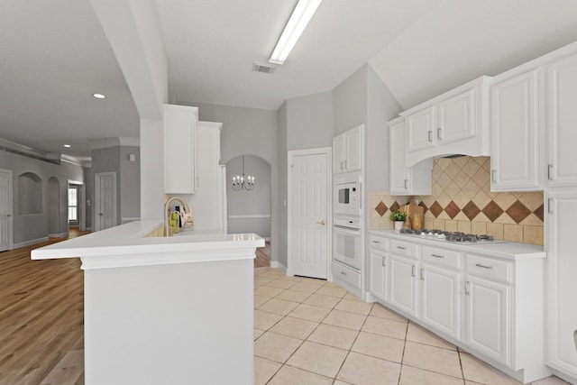 kitchen with visible vents, decorative backsplash, a peninsula, arched walkways, and white appliances