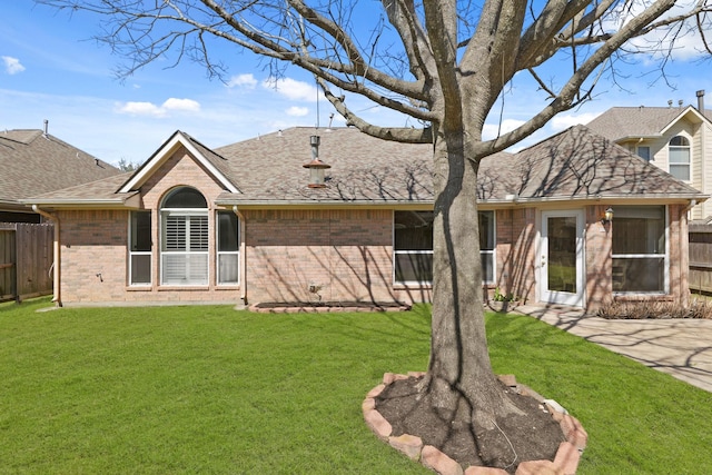 rear view of property with brick siding, a lawn, a shingled roof, and fence