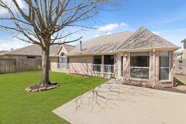 rear view of house featuring a yard, fence, brick siding, and roof with shingles