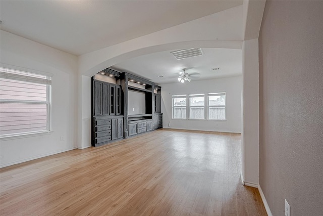 unfurnished living room featuring visible vents, arched walkways, light wood-style floors, baseboards, and ceiling fan