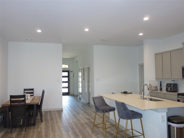 kitchen with light wood-style flooring, gray cabinetry, a sink, light countertops, and a kitchen breakfast bar