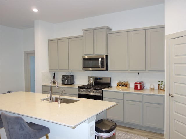 kitchen with a sink, stainless steel appliances, a kitchen breakfast bar, and gray cabinetry