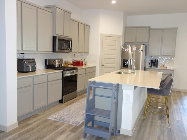 kitchen featuring backsplash, light wood-type flooring, gray cabinets, appliances with stainless steel finishes, and a sink