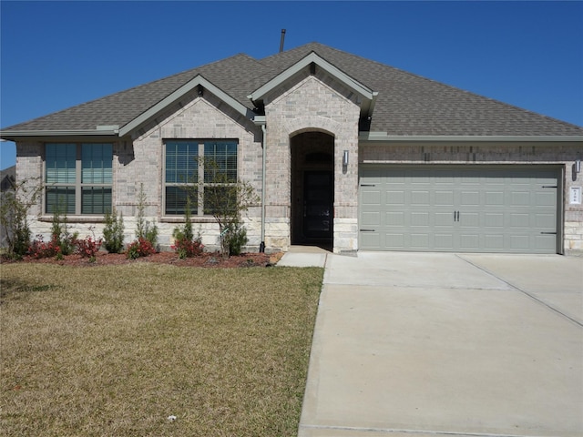 french country style house with brick siding, a shingled roof, a front lawn, a garage, and driveway