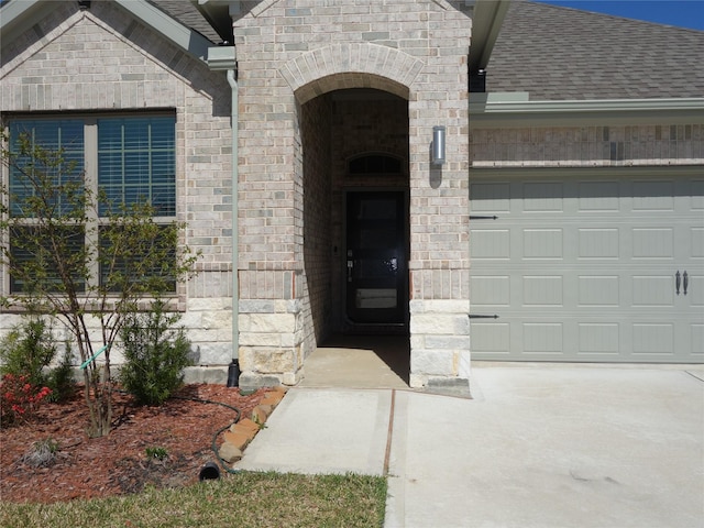 doorway to property with brick siding, an attached garage, and a shingled roof