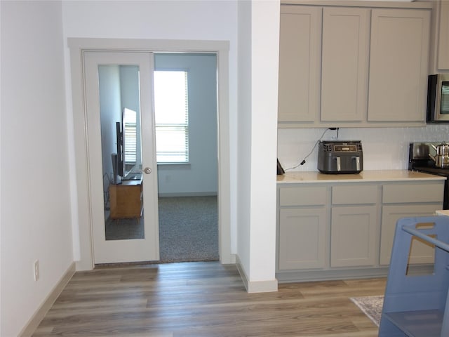 kitchen featuring decorative backsplash, light countertops, black electric range, and light wood-style floors