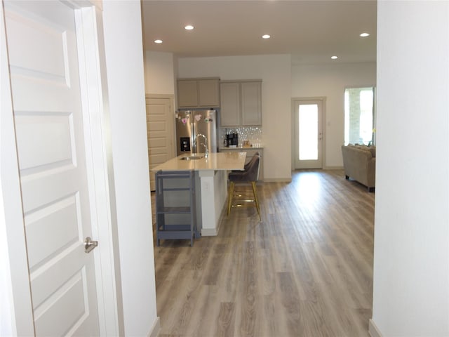 kitchen featuring gray cabinetry, stainless steel fridge with ice dispenser, a kitchen bar, light wood-style flooring, and a sink