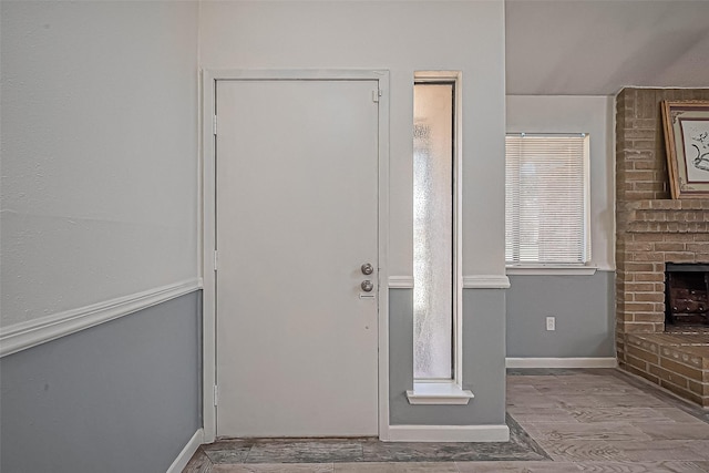 entrance foyer with a brick fireplace, wood finished floors, and baseboards