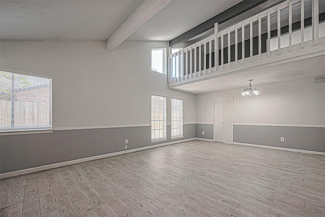 spare room with an inviting chandelier, beamed ceiling, wood finished floors, and a healthy amount of sunlight