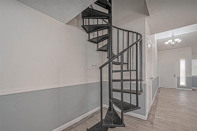 stairway with a notable chandelier, a textured ceiling, wood finished floors, baseboards, and a textured wall