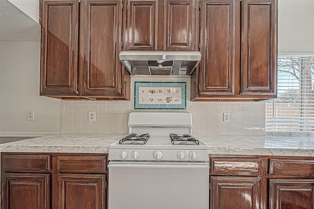 kitchen with tasteful backsplash, dark brown cabinetry, wall chimney exhaust hood, and white gas range oven