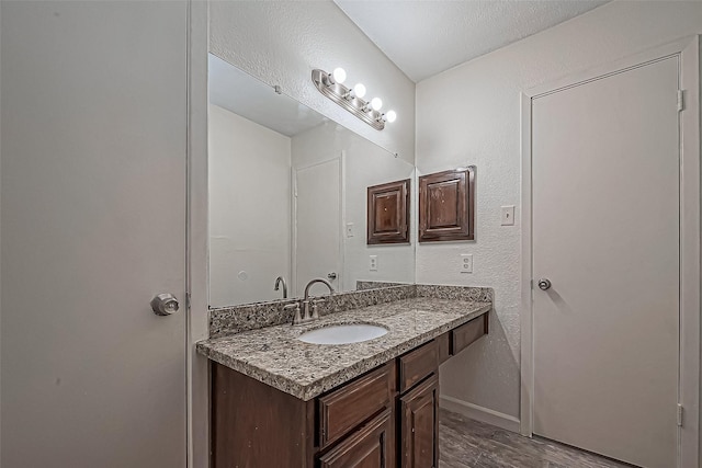 bathroom featuring vanity, wood finished floors, baseboards, and a textured wall