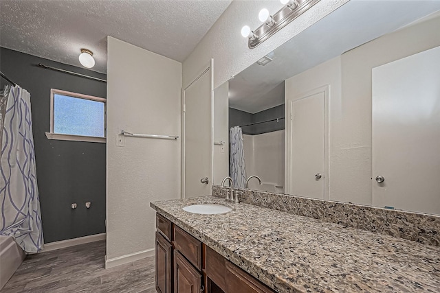 full bath with vanity, wood finished floors, visible vents, baseboards, and a textured ceiling