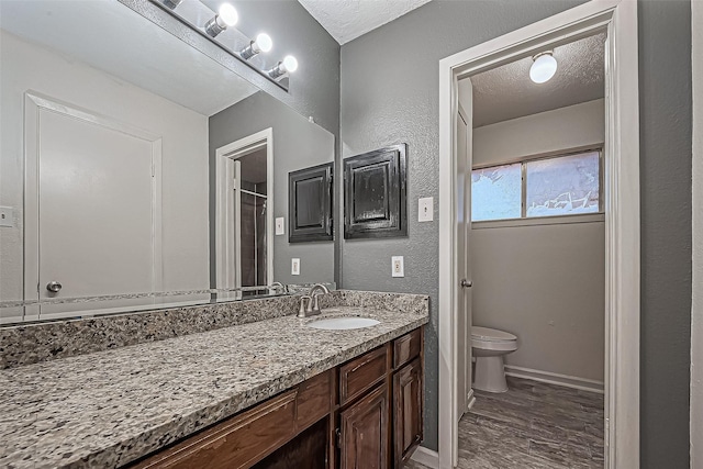 bathroom with toilet, vanity, wood finished floors, a textured wall, and a textured ceiling