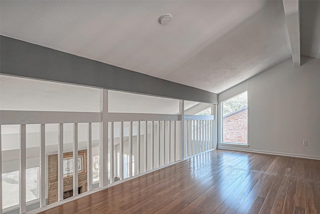 unfurnished room featuring baseboards, wood finished floors, and vaulted ceiling with beams