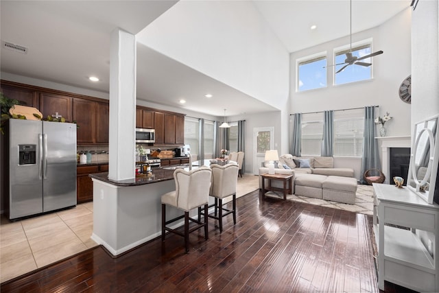 kitchen with visible vents, a breakfast bar area, a fireplace, wood finished floors, and stainless steel appliances