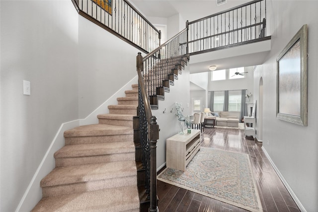 stairway with baseboards, a high ceiling, wood finished floors, and a ceiling fan