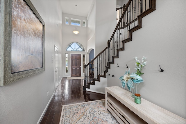 entryway featuring a towering ceiling, baseboards, wood finished floors, and stairs