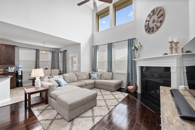 living area with light wood-type flooring, a towering ceiling, baseboards, ceiling fan, and a tile fireplace