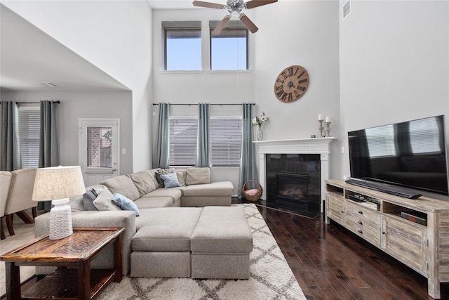 living room with visible vents, a fireplace, ceiling fan, dark wood-type flooring, and a towering ceiling