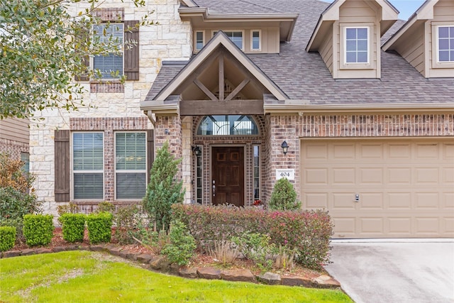 doorway to property with brick siding, stone siding, an attached garage, and a shingled roof