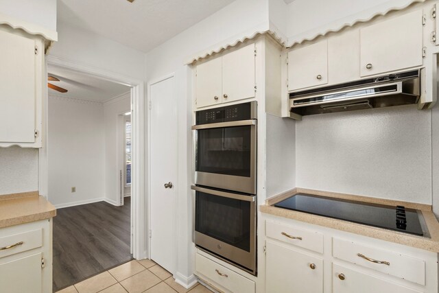 kitchen featuring light tile patterned floors, stainless steel double oven, light countertops, under cabinet range hood, and black electric cooktop