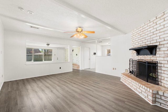 unfurnished living room with a ceiling fan, wood finished floors, visible vents, a fireplace, and a textured ceiling