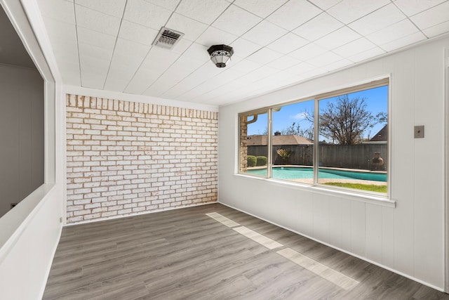 spare room with visible vents, wood finished floors, and brick wall