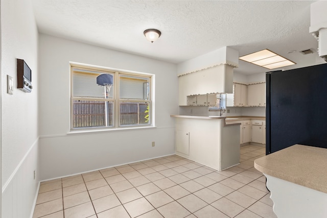 kitchen with light countertops, a peninsula, freestanding refrigerator, light tile patterned flooring, and a textured ceiling