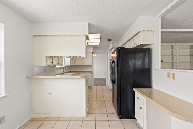 kitchen with light tile patterned floors, a peninsula, freestanding refrigerator, light countertops, and a textured ceiling