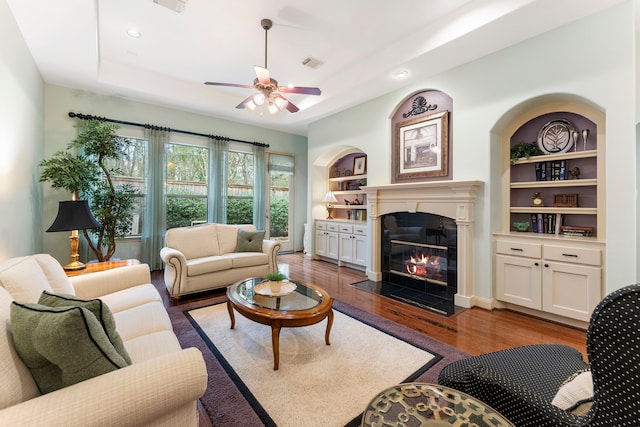 living room with visible vents, dark wood finished floors, a fireplace with flush hearth, a tray ceiling, and a ceiling fan