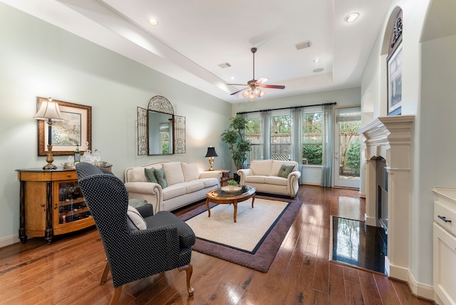 living room with visible vents, a tray ceiling, a fireplace with flush hearth, ceiling fan, and wood-type flooring