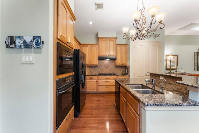 kitchen with backsplash, under cabinet range hood, dark wood finished floors, black appliances, and a sink