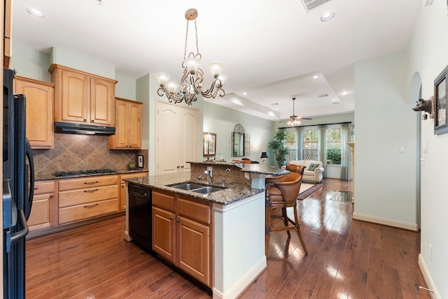 kitchen with a breakfast bar area, an island with sink, a sink, black appliances, and under cabinet range hood