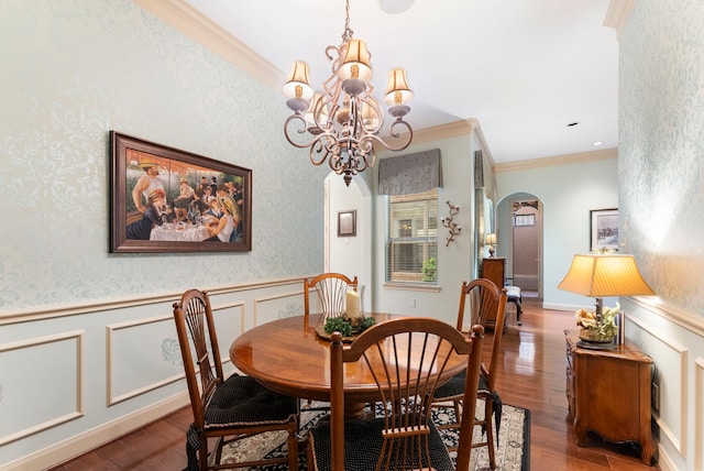 dining room featuring a wainscoted wall, ornamental molding, wood finished floors, arched walkways, and wallpapered walls