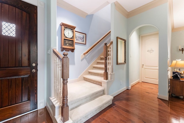 entryway featuring stairway, wood finished floors, baseboards, arched walkways, and crown molding